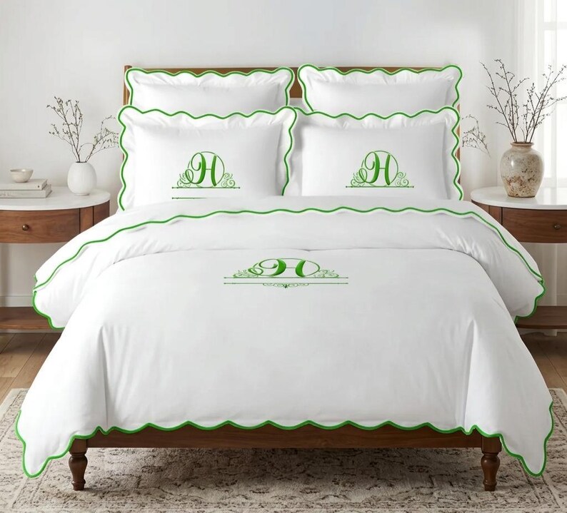 May include: A white bedding set featuring a scalloped green trim and a green embroidered letter H monogram centered on the duvet cover and two pillowcases. The set includes two additional plain white pillowcases with matching green scalloped edges.