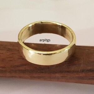 May include: A gold-colored ring with a smooth, polished surface. The ring is set on a dark wooden surface. The text "arpitgs" is visible on the ring.