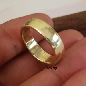 May include: A gold-colored ring with a smooth, polished surface. The ring has a rounded band and a simple, classic design. The ring is held in a hand, and the text "arpitgs" is visible.