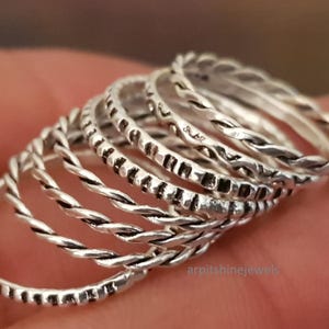 May include: A selection of silver rings with diverse textures, including twisted and patterned designs. The rings are stacked, highlighting their varied styles and intricate details. The rings are a jewelry item.