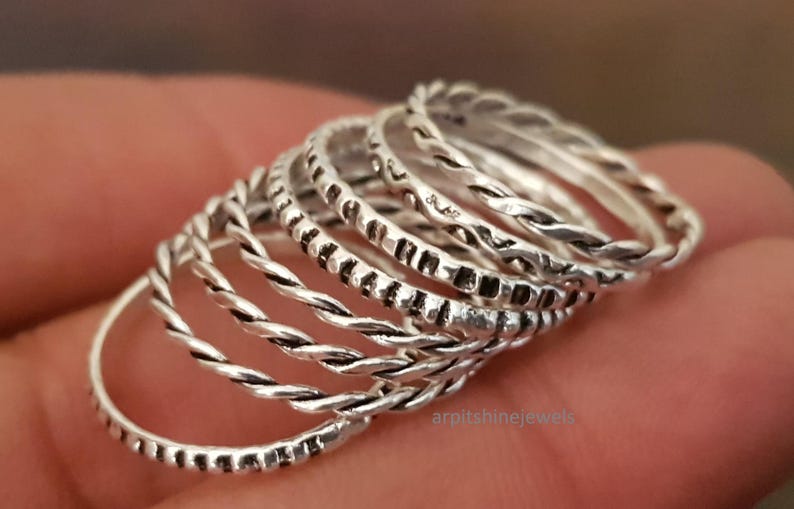 May include: A selection of silver rings with diverse textures, including twisted and patterned designs. The rings are stacked, highlighting their varied styles and intricate details. The rings are a jewelry item.
