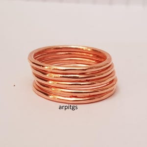 May include: A stack of copper-colored rings. The rings have a hammered texture and are stacked together. The rings are on a white surface. The text "arpitgs" is visible on the bottom right.