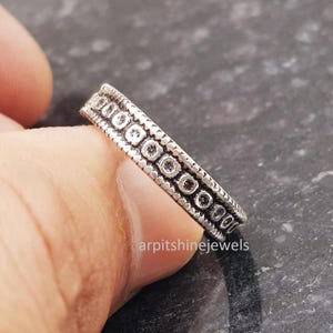 May include: A silver ring with a repeating pattern of small circles and dots. The ring is held by a person's finger. The ring has a textured design and is likely made of sterling silver. The ring is a piece of jewelry.