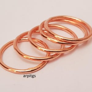 May include: A collection of copper-colored rings, each with a simple, rounded design. The rings are stacked and slightly overlapping, creating a layered effect. The rings are on a white background. The text "arpitgs" is visible in the lower left corner.