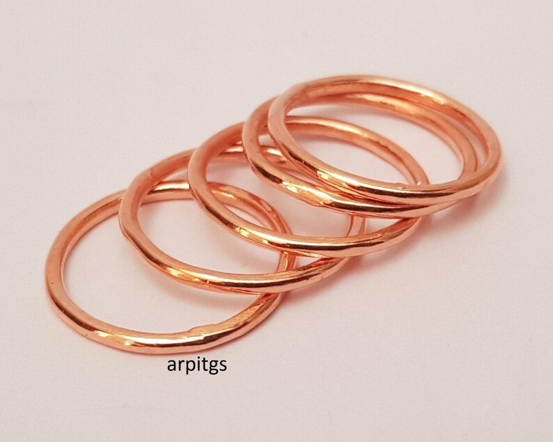 May include: A collection of copper-colored rings, each with a simple, rounded design. The rings are stacked and slightly overlapping, creating a layered effect. The rings are on a white background. The text "arpitgs" is visible in the lower left corner.