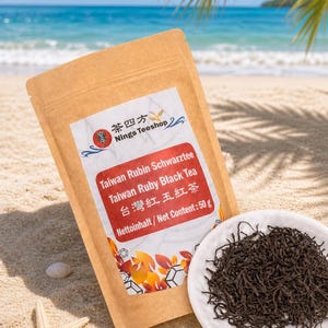 Könnte beinhalten: Ein braunes Papierpaket mit Taiwan Ruby Schwarztee von Nings Teeshop, mit Text in Englisch und Chinesisch, liegt am Sandstrand. Daneben ein kleiner weißer Teller mit losem Tee.