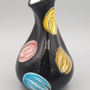May include: A glossy black ceramic vase with a teardrop shape and a narrow neck. The exterior features scattered, hand-painted circular motifs in yellow, pink, and blue, each containing fine, swirling white line details throughout the surface.