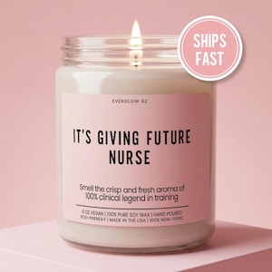May include: A lit candle in a glass jar with a pink label. The label reads "IT'S GIVING FUTURE NURSE" and includes text about the scent and ingredients. A "SHIPS FAST" sticker is on the right.