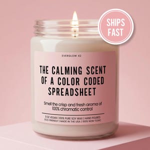 May include: A lit candle in a glass jar with a pink label. The label reads "THE CALMING SCENT OF A COLOR CODED SPREADSHEET." The candle is 9 oz and made with vegan soy wax. A pink circle with "SHIPS FAST" is in the upper right.