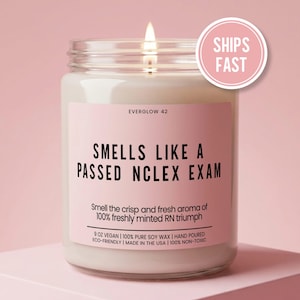 May include: A clear glass jar candle with a lit wick and a pink label. The label reads EVERGLOW 42, SMELLS LIKE A PASSED NCLEX EXAM, Smell the crisp and fresh aroma of 100% freshly minted RN triumph, 9 OZ VEGAN, 100% PURE SOY WAX, HAND POURED, ECO-FRIENDLY, MADE IN THE USA, 100% NON-TOXIC.