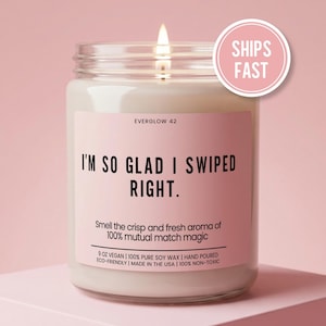 May include: A lit, clear glass jar candle with a pink label that reads "I'M SO GLAD I SWIPED RIGHT." The candle is labeled "EVERGLOW 42" and includes the text "Smell the crisp and fresh aroma of 100% mutual match magic." A pink circle with "SHIPS FAST" is on the right.