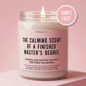 May include: A lit, glass jar candle with a pink label that reads "THE CALMING SCENT OF A FINISHED MASTER'S DEGREE." The candle is labeled "EVERGLOW 42" and includes text about the scent and ingredients. A pink circle with "SHIPS FAST" is in the upper right.