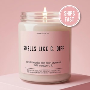 May include: A lit, white candle in a glass jar with a pink label. The label reads "SMELLS LIKE C. DIFF" and "Smell the crisp and fresh aroma of 100% isolation chic." A pink circle with "SHIPS FAST" is in the upper right.