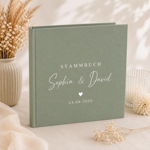 Könnte beinhalten: Ein salbeigrünes, quadratisches Buch mit Stoffeinband, das auf der Vorderseite den weißen Aufdruck STAMMBUCH, die Namen Sophia & David in Schreibschrift, ein kleines Herzsymbol sowie das Datum 24.08.2026 auf dem festen Einband zeigt.