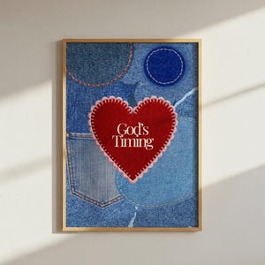 Puede incluir: Una impresión artística enmarcada que presenta un collage de varias texturas de tela vaquera azul, incluyendo un bolsillo y parches circulares. Centrado hay un gran aplique de fieltro rojo en forma de corazón con bordes festoneados blancos y el texto God's Timing.