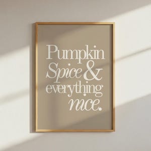 Könnte beinhalten: Ein rechteckiger Wandkunstdruck in einem hellen Holzrahmen mit beigem Hintergrund und dem weißen Text Pumpkin Spice & everything nice. Die Typografie besteht aus einer Mischung aus fetten Serifenschriften und eleganten Schreibschriften.