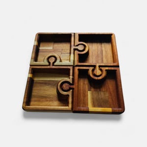 Peut inclure: Plateau de service en bois en forme de puzzle en quatre parties. Chaque plateau carré est d'une nuance de brun différente et se connecte aux autres avec un design de pièce de puzzle. Les plateaux ont une forme carrée avec une zone encastrée.