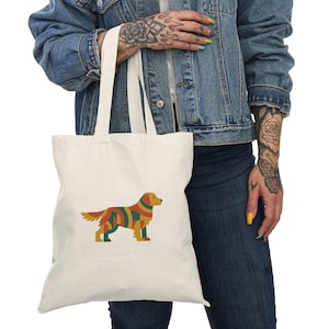 Può includere: Borsa tote color crema con un colorato design geometrico di un cane. L'illustrazione del cane utilizza sfumature di giallo, rosso, verde e arancione. La borsa ha due manici bianchi ed è realizzata in un tessuto resistente.