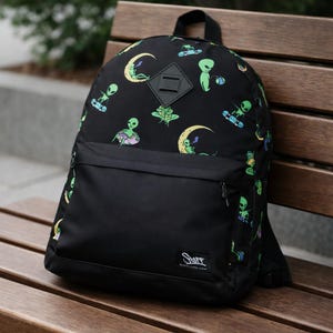 May include: Black backpack with a large front pocket and a top handle. The backpack features a pattern of green aliens, yellow moons, and other colorful graphics. The word "Stuff" is printed on the bottom right of the front pocket.