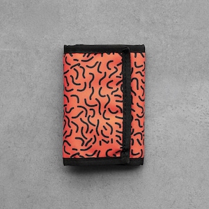May include: A tri-fold wallet featuring an orange pattern of black squiggles. The edges and the strap are black. The wallet is closed and rests on a grey surface. The wallet is approximately 10 cm in length.