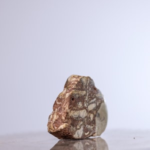 Puede incluir: Una piedra natural con un patrón moteado de marrón, beige y blanco. La piedra tiene una superficie rugosa y texturizada y una forma irregular. Es probable que sea un objeto decorativo o una obra de arte natural.