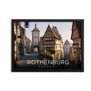 May include: A framed wall art print featuring a street scene in Rothenburg, Germany, with half-timbered buildings and a clock tower. The text ROTHENBURG GERMANY is printed in white at the bottom centre of the image within a black frame.