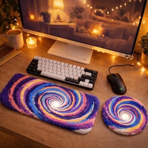 May include: A desk setup featuring a keyboard, mouse, and a colorful, spiral-patterned mousepad and coaster. The mousepad and coaster have a vibrant design with shades of purple, blue, orange, and yellow. The keyboard is black and white.