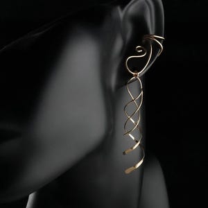 May include: A gold-toned ear cuff featuring a double-wire band that wraps around the upper ear cartilage, connected to a long, dangling spiral wire element that extends downwards in a series of interconnected, open-loop twists.