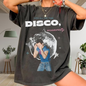 May include: Dark gray t-shirt with the words "DISCO, occasionally" and "Kiss all the time" printed on the front. The shirt features a graphic of a man in front of a disco ball. The shirt is a vintage style.