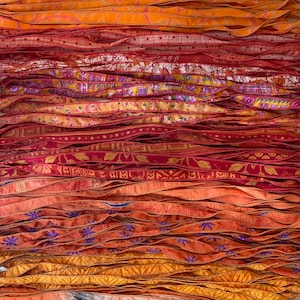 Puede incluir: Una colección de cintas de tela dispuestas horizontalmente en varios tonos de naranja, rojo y amarillo. Las cintas presentan diversos patrones, incluyendo motivos florales, formas geométricas y estampados abstractos, con texturas y costuras detalladas.