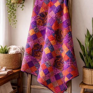 May include: A vibrant, patchwork quilt draped over a wooden ladder. The quilt features a mix of purple, orange, and red squares with intricate floral patterns. The quilt's edges are finished with a deep purple border, creating a cozy and colorful home decor item.