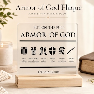 Può includere: Una targa in acrilico trasparente su base in legno chiaro con testo e icone nere che rappresentano l'armatura di Dio. Il testo recita Put on the full Armor of God, elencando Belt of Truth, Breastplate of Righteousness, Shoes of Peace, Shield of Faith, Helmet of Salvation, Sword of Spirit e Ephesians 6:10.