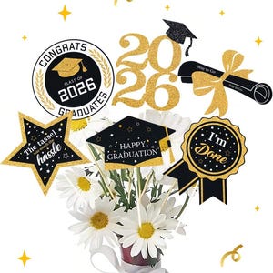 Könnte beinhalten: Ein Strauß weißer Gänseblümchen in einer roten Vase, verziert mit glitzernden goldenen und schwarzen Dekorationen zum Thema Abschluss. Die Dekorationen zeigen das Jahr "2026", eine Doktorhut und Sätze wie "Herzlichen Glückwunsch an die Absolventen" und "Ich bin fertig".