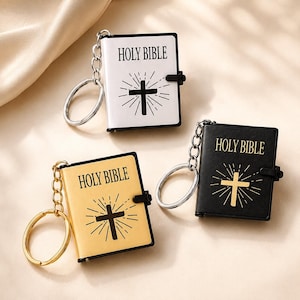 May include: Three miniature book keychains featuring the text HOLY BIBLE and a cross graphic. One keychain is white with a black cross, one is black with a gold cross, and one is gold with a black cross. Each includes a metal ring and chain.