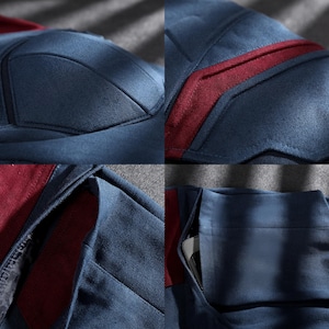 May include: Close-up of a navy blue garment with burgundy detailing. The fabric has a textured finish, with visible stitching and paneling. Features include a pocket and reinforced seams, indicating a tailored design.