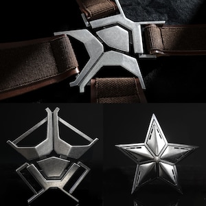 May include: Close-up of metal buckles and a star-shaped emblem. The silver buckles are attached to brown fabric straps. The star emblem is also silver and has a detailed, multi-faceted design. These appear to be costume or prop pieces.