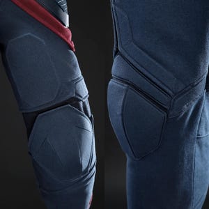May include: Close-up of navy blue protective gear, possibly for sports or tactical use. The gear features padded sections with geometric stitching, offering enhanced protection. The design incorporates a combination of navy blue and black materials.
