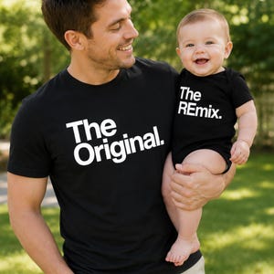 May include: A black short-sleeved t-shirt with the white text The Original. and a matching black short-sleeved baby bodysuit with the white text The REmix. The text is printed in a bold, sans-serif font on the front of each garment.