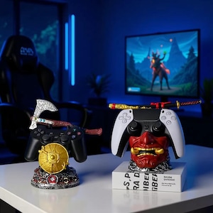 Puede incluir: Dos mandos de juego negros con bases decorativas. Un mando tiene un hacha plateada y un escudo dorado. El otro mando tiene una máscara Oni roja y dorada y una katana. Los mandos están sobre una superficie blanca.