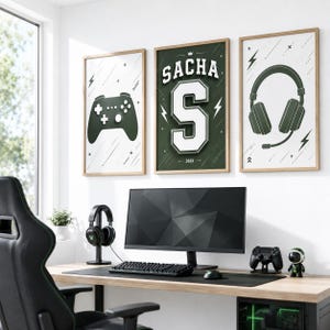 Pode incluir: Três quadros decorativos com moldura apresentando um comando de jogo verde-escuro, o nome SACHA acima de uma letra S grande e um headset verde-escuro. Os designs incluem raios brancos e detalhes geométricos sobre fundo branco e verde.