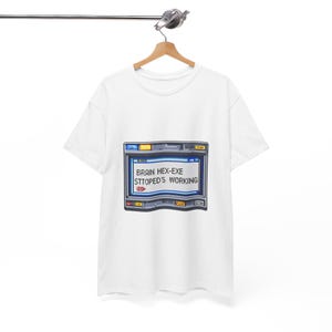 Op de afbeelding: Wit T-shirt met een afbeelding van een computerscherm met de tekst "BRAIN HEX-EXE STTOPED'S WORKING". Het scherm heeft een blauw en grijs ontwerp met rode en gele accenten. Het T-shirt hangt aan een houten hanger.