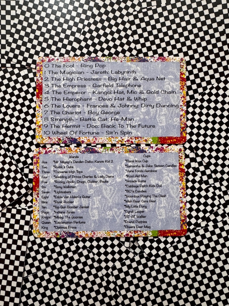May include: Two rectangular cards with a light blue background and a colourful paint-splatter border. The cards feature lists of tarot-style titles paired with 1980s pop culture references, including The Fool, The Magician, Wands, and Cups.