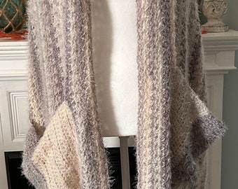 May include: A soft, striped, fuzzy knit scarf with a pocket and fringe. The scarf is in shades of grey, white, and beige.