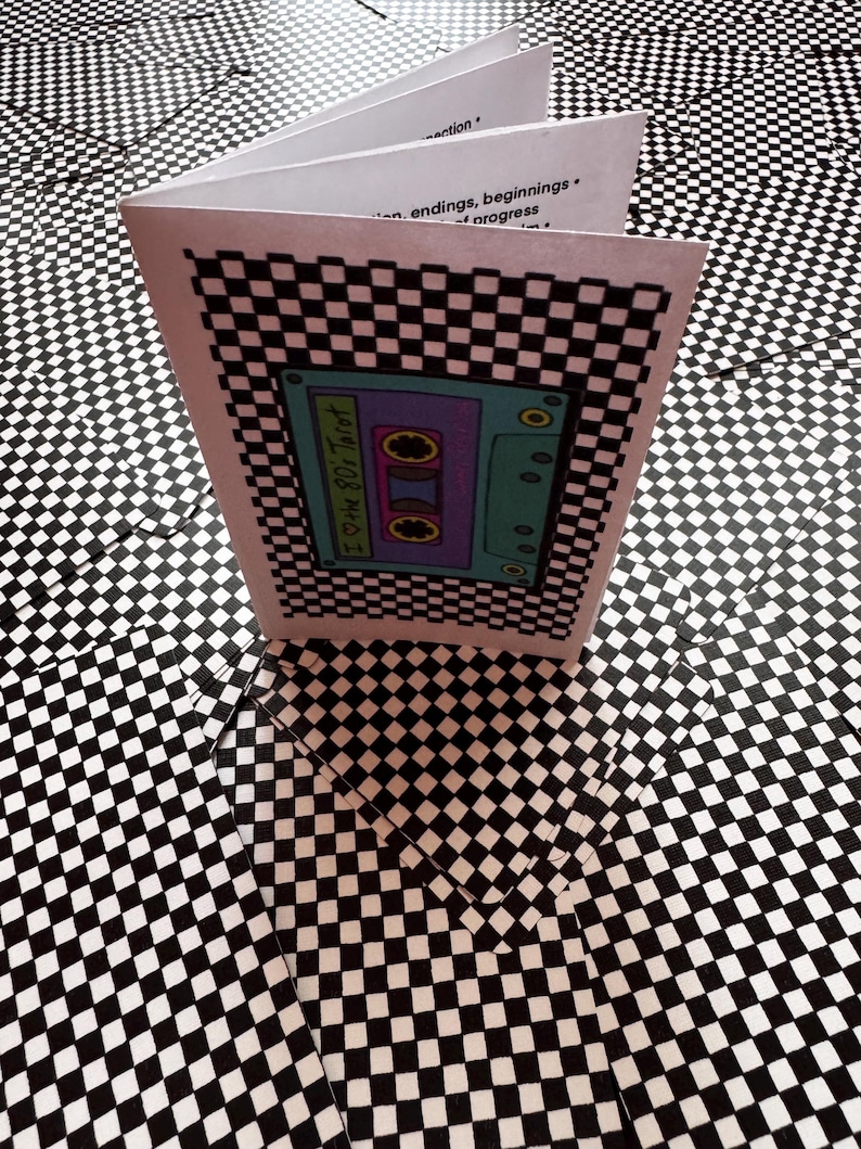 May include: A small white booklet with a black and white chequered border and a central illustration of a teal cassette tape labelled I Love the 80s Tarot. The interior pages show printed text including the words connection, endings, beginnings, and progress.