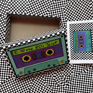 May include: A tarot card deck box and a small booklet featuring a black and white chequerboard pattern. The box lid displays a colourful illustration of a cassette tape with the text I Love the 80's Tarot by Christy Plummer Reynosa.