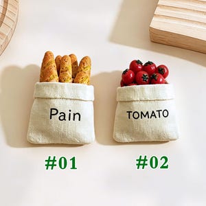 May include: Two small, off-white fabric bags with the words "Pain" and "TOMATO" printed on them. One bag contains several pieces of bread, and the other is filled with red tomatoes. The bags are labeled #01 and #02.