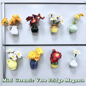 May include: A collection of eight mini ceramic vase fridge magnets, each holding colorful artificial flowers. Vases come in various colors, including white, yellow, black, and blue. The text "Mini Ceramic Vase Fridge Magnets" is at the bottom.