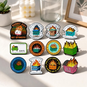 Puede incluir: Una colección de doce pines de esmalte con varios diseños de contenedores de basura en llamas. Los pines incluyen textos como "Burnt Out But Optimistic", "This Little Light of Mine", "Dumpster Fire Response Team" e "It's Fine", con coloridas ilustraciones de contenedores.