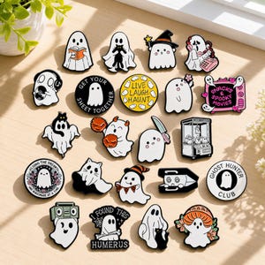 Puede incluir: Una colección de veinte pines de esmalte con varios diseños de fantasmas. Los pines incluyen fantasmas leyendo libros, sosteniendo gatos, usando sombreros, usando teléfonos, viendo televisión, sosteniendo cuchillos y escuchando música, con textos como Live Laugh Haunt.