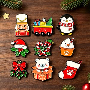 May include: A collection of nine colourful enamel pins featuring holiday themes including a nutcracker, a train with gifts, a penguin, a Santa hat with holly, candy canes, a snowman cupcake, mistletoe, a polar bear in a box, and a stocking.